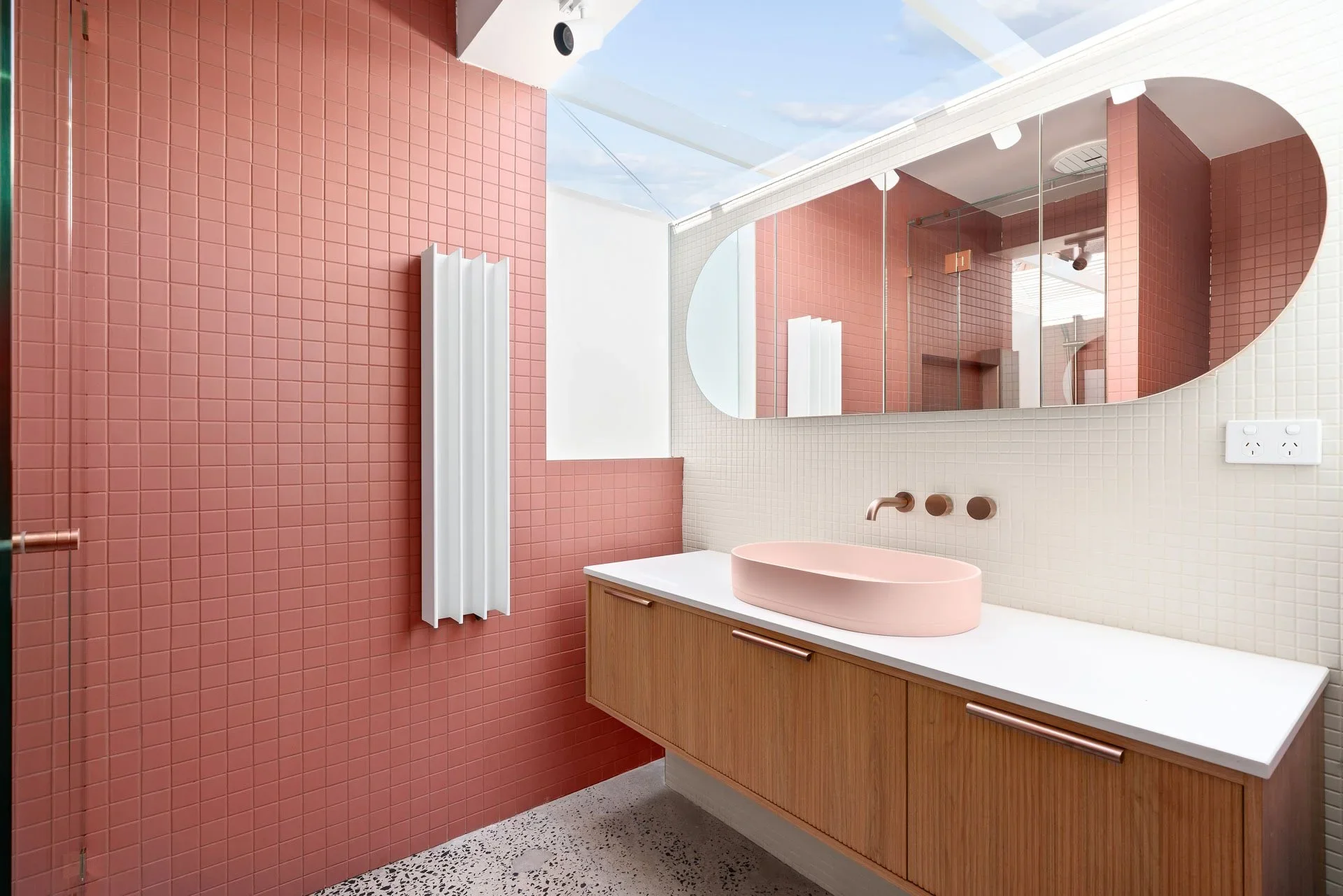 Pink square-tiled bathroom with round mirror, timber vanity and skylight, Hotham Street Beaumaris — Eco Building Design