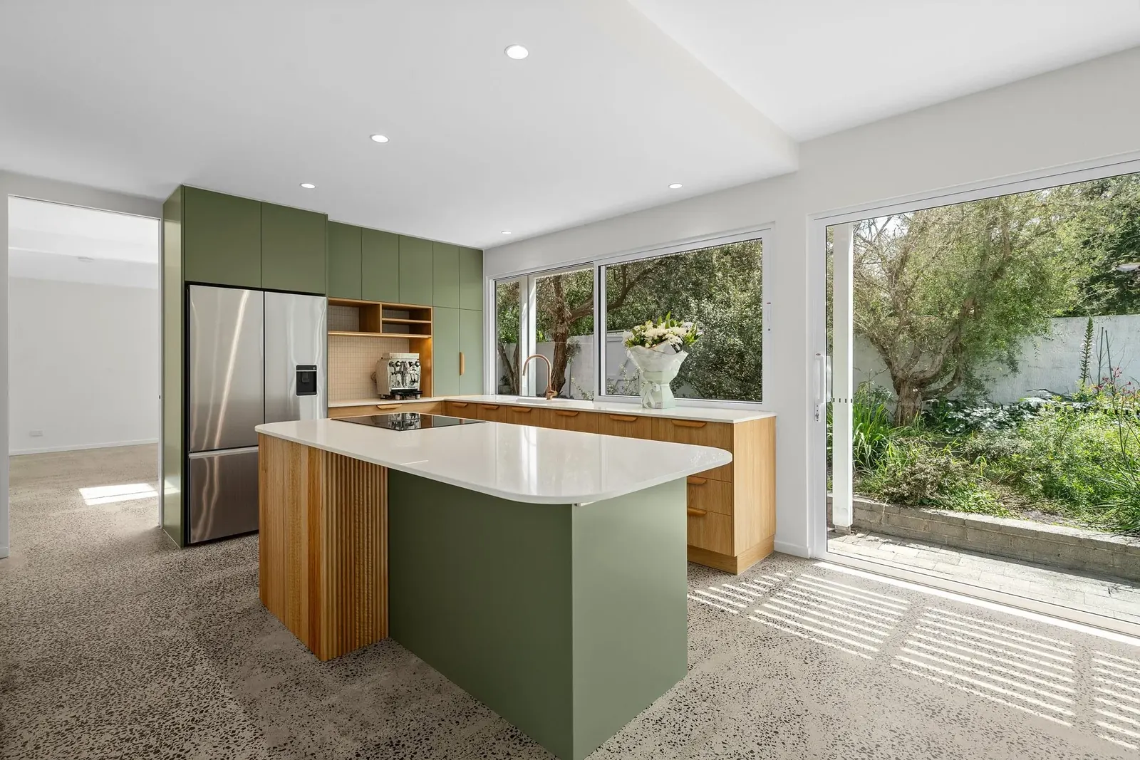 Sage-green and timber kitchen with curved island, fluted panels and garden outlook, Hotham Street Beaumaris — Eco Building Design